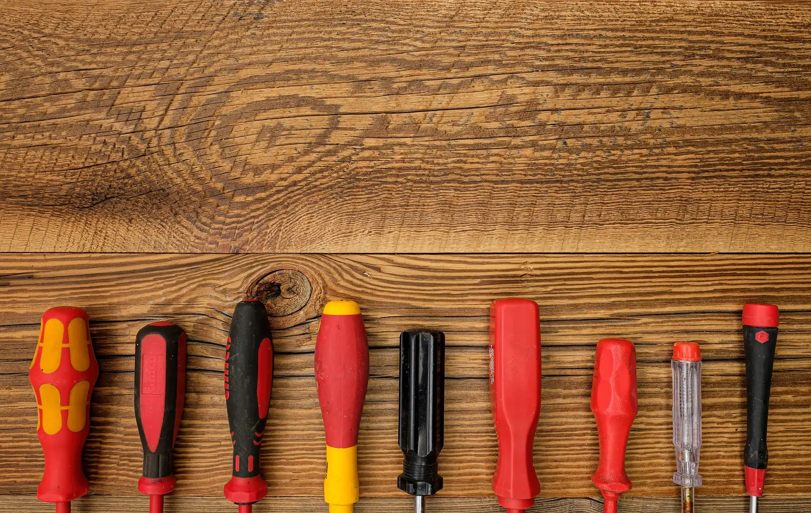 A row of screwdrivers lined up on a wooden bench.